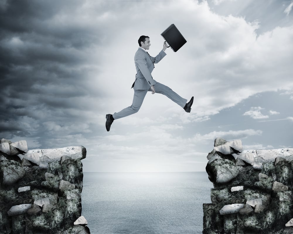 Businessman jumping a gap between cliffs with the sea on the background-1