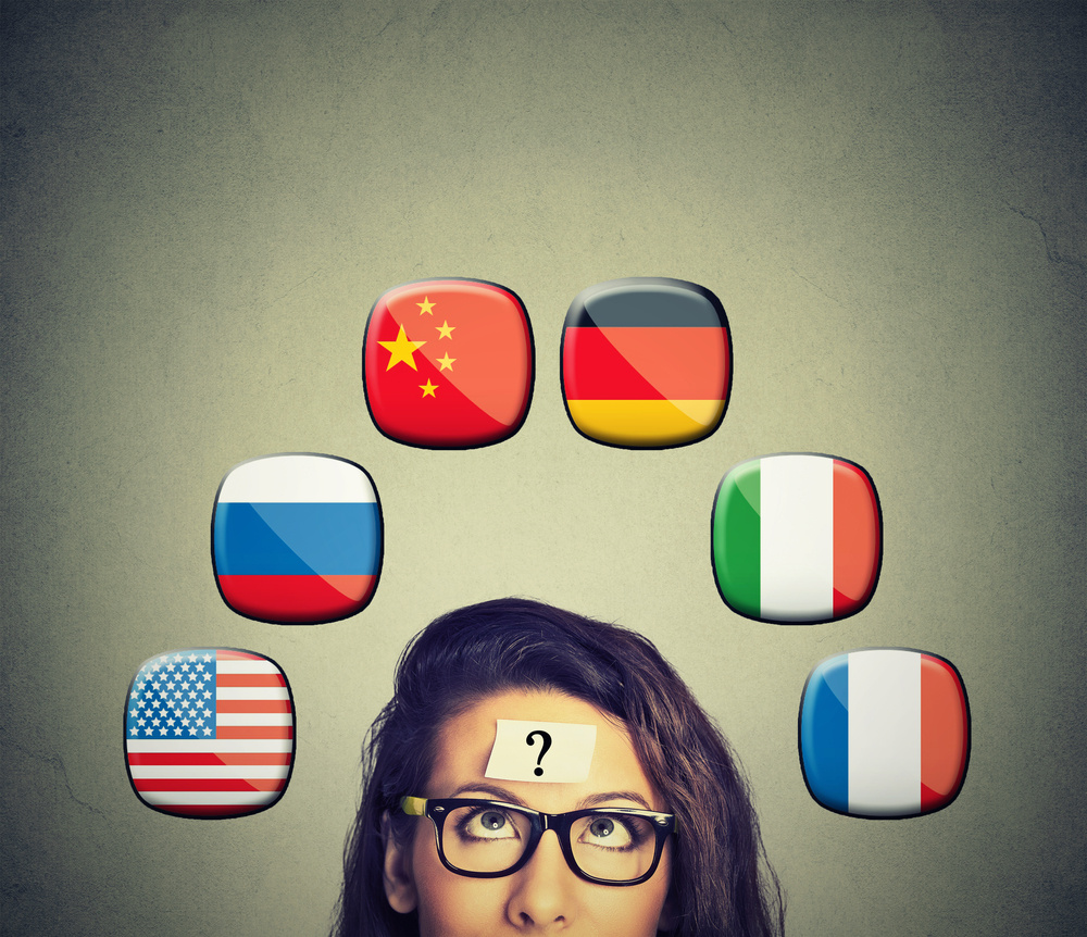 Work and travel immigration opportunity concept. Foreign language studying process. Woman with question mark and icons of international flags above head isolated on gray wall background.